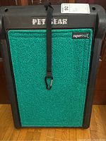 Front view of the green textured pet pad secured on black plastic frame with branding and strap visible.
