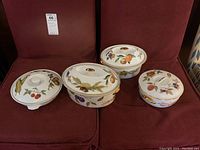 Four Royal Worcester Evesham lidded casserole dishes on red upholstery, showing fruit designs on lids and sides.