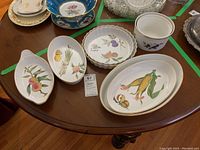 Eight ceramic Royal Worcester Evesham dishes and bowls on wooden table, featuring fruit and vegetable hand-painted designs with gold trim.