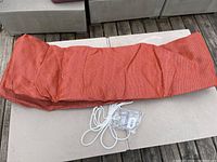 Red woven fabric sail tarp folded on a table with white rope and hardware kit packed in plastic bags.