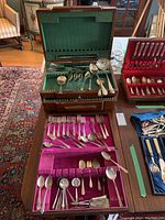 Overall view of three wooden cutlery cases containing assorted silver plate cutlery of various patterns and types placed on a table.