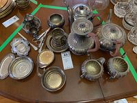 Top-down view of entire silver plate collection showing teapots, cream and sugar containers, serving utensils, and coasters arranged on wooden table.