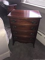 Front view of the small wooden dresser showing 4 drawers with metal handles and a glass top under natural light.