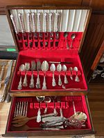 Open case showing lid with eight knives and two small spoons, middle slide-out tray above bottom compartment with forks, spoons and serving pieces.