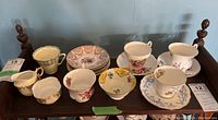 Overall lot on wooden shelf showing multiple teacups and saucers including cream and sugar set