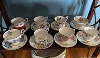 Eight assorted floral patterned teacups and saucers arranged in two rows on a shelf