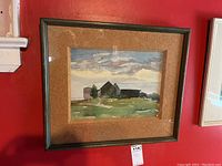 Framed watercolour painting hung on red wall showing rural buildings with cork board mount and visible frame wear.