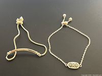 Pair of two Kendra Scott adjustable bracelets laid out flat on a black background, showing one gold-toned with bar and cubic zirconia accents and one silver tone with oval lattice centerpiece.