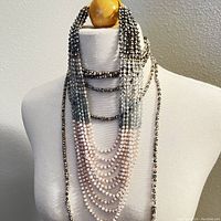 Two multicolored seed bead necklaces displayed on a white mannequin bust, showing their layered, glossy bead appearance with mixed shades of black, white, grey, and blush pink.