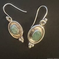 Pair of sterling silver earrings with oval blue-green turquoise stones in bezel settings on hook backs shown on black background