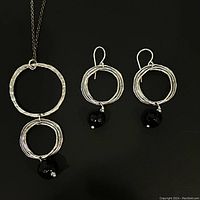 Photo of sterling silver necklace and earrings set showing hammered circle designs with black onyx beads on a black background.