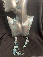 Full view of necklace and earrings on a mannequin showing blue aqua dyed natural shell mosaic pieces and beads on silver tone chain.
