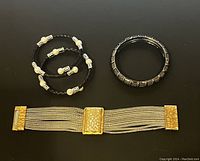 Three bracelets shown together on black background including braided leather pearl bracelets, black tone Cookie Lee bracelet, and multi-strand gold/silver rhinestone bracelet.