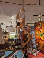 Photo shows a large Brutalist style candle holder hanging in an antique or vintage store environment, surrounded by other items. The holder is metal, with a rusty-bronze patina and multiple open cutouts creating an abstract and sculptural shape.