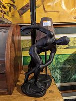 Bronze-colored sculpture lamp depicting a discus thrower in a dynamic pose with lamp stand and shade attached, displayed on a wooden surface.