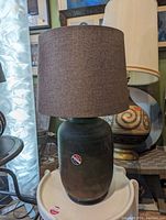 Full view of mid-century ceramic lamp showing the dark brown fabric shade and dark glazed ceramic base with manufacturer stickers