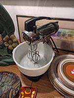 Electric stand mixer with white mixing bowl, two metal beaters attached, chrome and black body.
