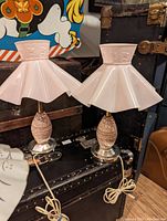 Pair of retro ceramic bedside lamps with pleated pink floral embossed shades and textured ceramic bases on metallic stands, placed on a black chest.