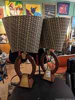 Pair of decorative lamps featuring circular wooden bases with brass detailing and patterned fabric shades in a mid-century style environment.
