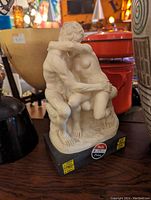 Photo of the R. Santini statue showing two nude figures embracing on a black base with price and sale stickers.