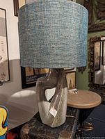 Front view of ceramic table lamp with abstract sculptural base and blue fabric cylindrical shade.