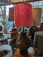 Photo of mid-century ceramic lamp with pink fabric shade on wooden table among other lamps.