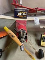 Front view of model airplane showing red fuselage, wooden propeller, FA-45 four-stroke engine, and cables.