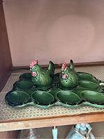 Two green ceramic chicken salt and pepper shakers placed on a matching green egg dish with twelve egg indentations, sitting on a shelf.