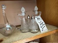 Two large etched glass dressing bottles with stoppers, pair of matching salt and pepper shakers, and glass swan figure on shelf