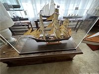 Full view of the wooden sailing ship inside the plexiglass case on a table