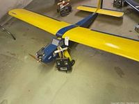 Blue and yellow model airplane with MRC series 765 remote control placed on the floor showing full top and side view of airplane and remote.