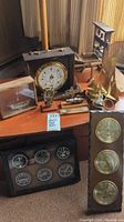 Photo showing large weather station with white dial, brass framed panel with three instruments, and various nautical decorative items on a table.