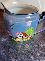 Close-up of creamer jug showing hand-painted cottage and bird design on iridescent blue background