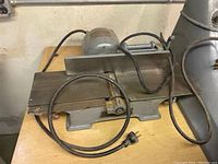 Photo of the first Walker-Turner power tool, a planer or driver-cutter with electric motor and attached power cord, sitting on a wooden table, shows metal base and some rust.