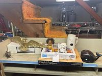 Photo showing a collection of figurines including brass eagle, small doll, white cat, ceramic pitcher, resin whale, and a boxed 'Playful Puppies' jigsaw puzzle set.