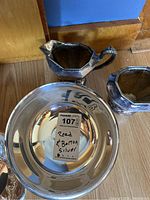 Photo showing hexagonal creamer, sugar container, and one silver bowl with a lot tag inside the bowl.