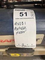 Close-up of the top of the planer with a label indicating 'RYOBI Portable Planer'. Shows part of carrying handle and tool's casing.