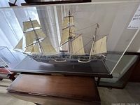 Full view of model ship inside plexiglass case on wooden base