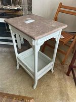 Full view of the small side table, showing pink marble top and white wooden decorative legs with lower shelf.