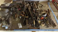 Photo showing assortment of hand tools and a bench grinder on a wooden surface, with various wrenches, clamps, pliers, screwdrivers, and other tools in view.