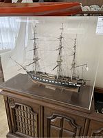 Front view of three-masted U.S.S. Constitution model inside clear plexiglass display case on wooden base