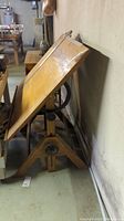 Side view of the vintage wooden drafting table showing angled top and wooden base with adjustment hardware.