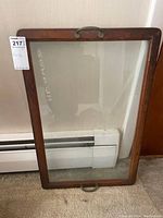 Full view of a vintage glass tray with wooden frame and curved metal handles on each end, showing clear glass surface and medium-tone wooden trim.