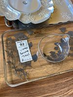 Close-up photo showing the two glass trays with floral leaf designs and one metal tray partially visible under them.