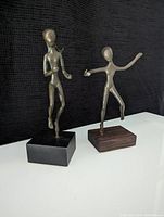Front view of two bronze sculptures on square bases against black fabric background