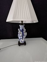 Full view of porcelain lamp with blue and white Chinoiserie design and attached baby figurines, topped with white fabric lampshade.