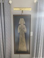 Framed medieval brass rubbing artwork with brass gallery lamp above lit to show detail.