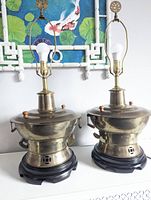 Pair of large brass Asian cooking vessel lamps shown on white surface with decorative background.