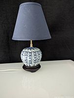 Full view of the vintage Chinoiserie blue and white gourd lamp turned off, showing porcelain base, wooden stand, and blue lampshade against black background.