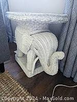 Side view of white wicker elephant plant stand showing detailed trunk and legs with shadow from nearby curtains.